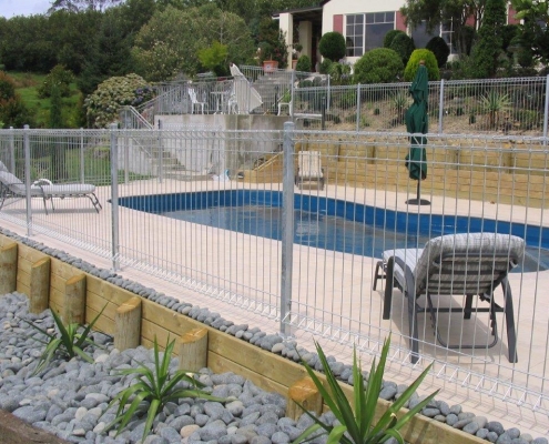 Image showing a kidney shaped residential swimming pool surrounded by pool fencing and landscaped gardens