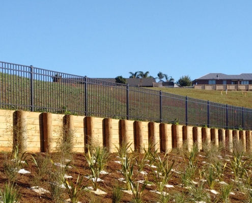 Image showing roadside native plants leading up to a retaining wall with balustrade at the top, in a new subdivision, installed by Fencerite