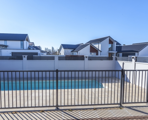 Image showing black aluminium pool fencing and gate, enclosing a modern swimming pool area in residential grounds