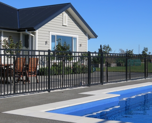 Image showing black aluminium pool fencing and gate, enclosing a modern swimming pool area in residential grounds
