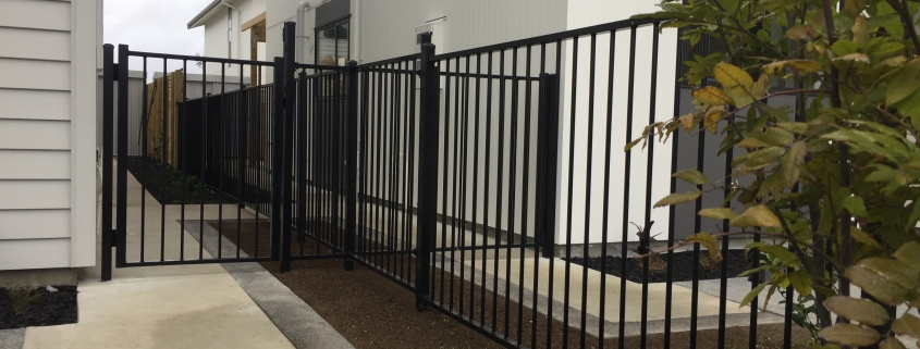 Image showing a black aluminium fence and gate separating two residential buildings, installed by Fencerite